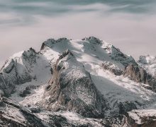 Snow-covered mountain range under cloudy sky Snowy mountain peaks with cloudy sky
